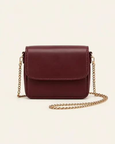 Mini borsa a tracolla bordeaux con catena dorata su fondo avorio